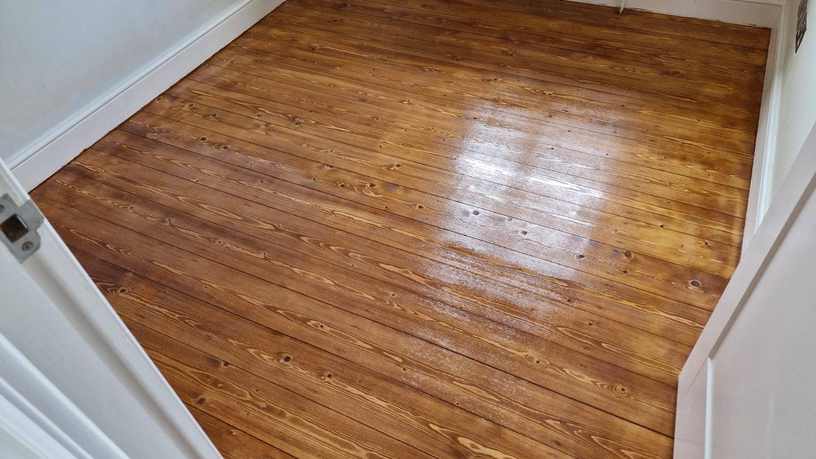 Room with a beautifully finished wooden floor after sanding and refinishing by Mr Sander®. The floor is glossy and smooth, enhancing the natural wood grain and warm tones. Location: Heathrow, UK. Floor type: Pinewood planks.