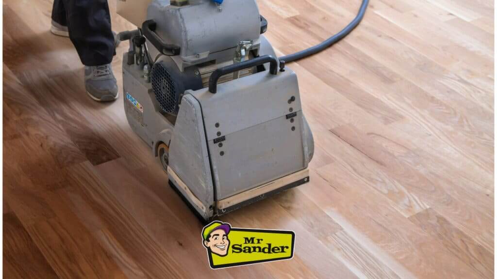 A professional from Mr Sander® is sanding a solid oak hardwood in a living room in Wickford, UK using a Bona Belt sander (AMO110000.3). The machine features a 2.2 kW motor, 230 V voltage, 50 Hz frequency, and a sanding belt size of 200 x 750 mm or 250 x 750 mm. The total weight is 74 kg.