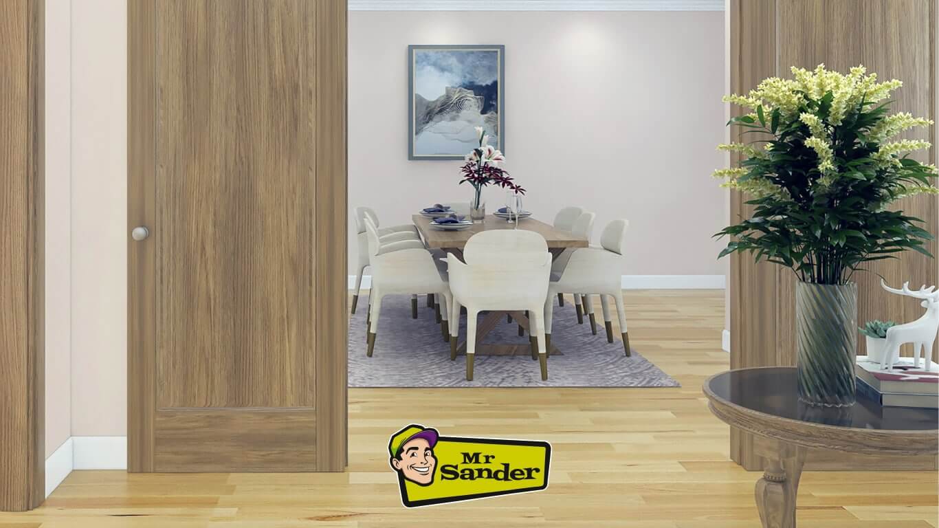 A dining room with a restored wood floor. The floor is sanded and refinished to a warm, honey-colored finish. The room features a dining table with chairs, a side table, and a vase of flowers. The Mr. Sander logo is visible in the lower right corner.