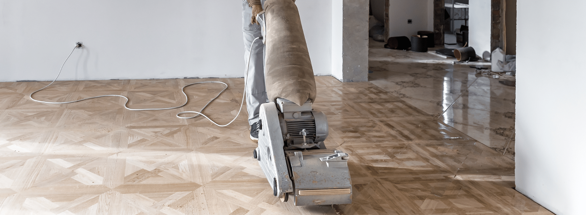 Mr Sander® meticulously sanding a herringbone floor using an Effect 2200 (220V, 50-40Hz) Bona belt sander in Poplar, E14. The 350x750 mm sander, connected to a HEPA-filtered dust extraction system, ensures a clean and efficient result for a flawless finish.