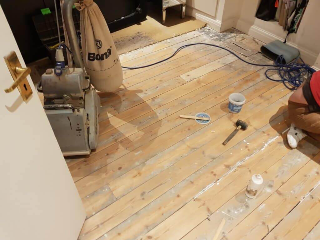 A professional from Mr Sander® is sanding a pine floor in a living room using a Bona Belt sander (AMO110000.3). The machine features a 2.2 kW motor, 230 V voltage, 50 Hz frequency, and a sanding belt size of 200 x 750 mm or 250 x 750 mm. The total weight is 74 kg.