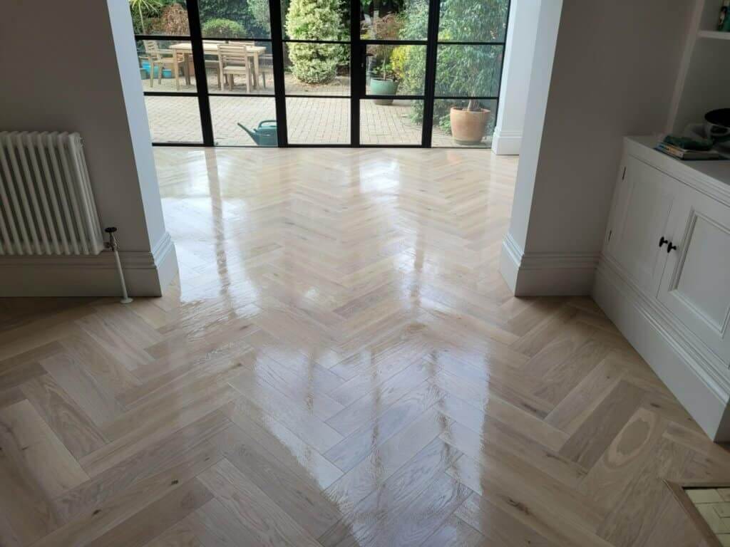 Beautifully refinished herringbone wood floor by Mr Sander® in Finchley Church End, UK. The polished floor gleams in the natural light coming through large glass doors leading to an outdoor patio.