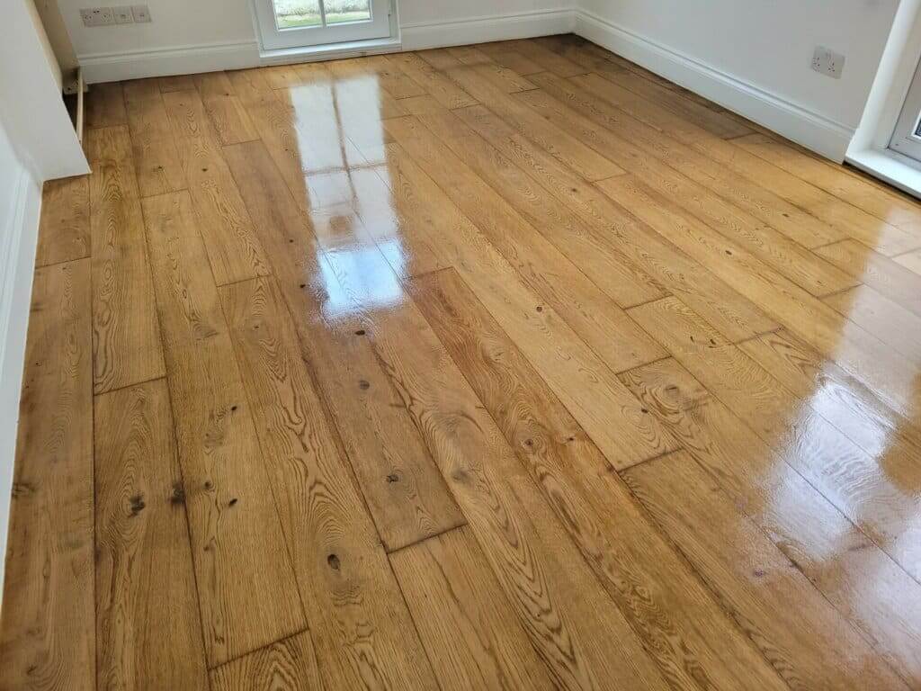 A close-up view of a stunningly refinished oak hardwood floor in Euston, UK. The image showcases the smooth, glossy finish and the rich, natural wood grain, highlighting the expert floor sanding and refinishing work by Mr Sander. The polished surface reflects light from a nearby window, emphasizing the professional craftsmanship.