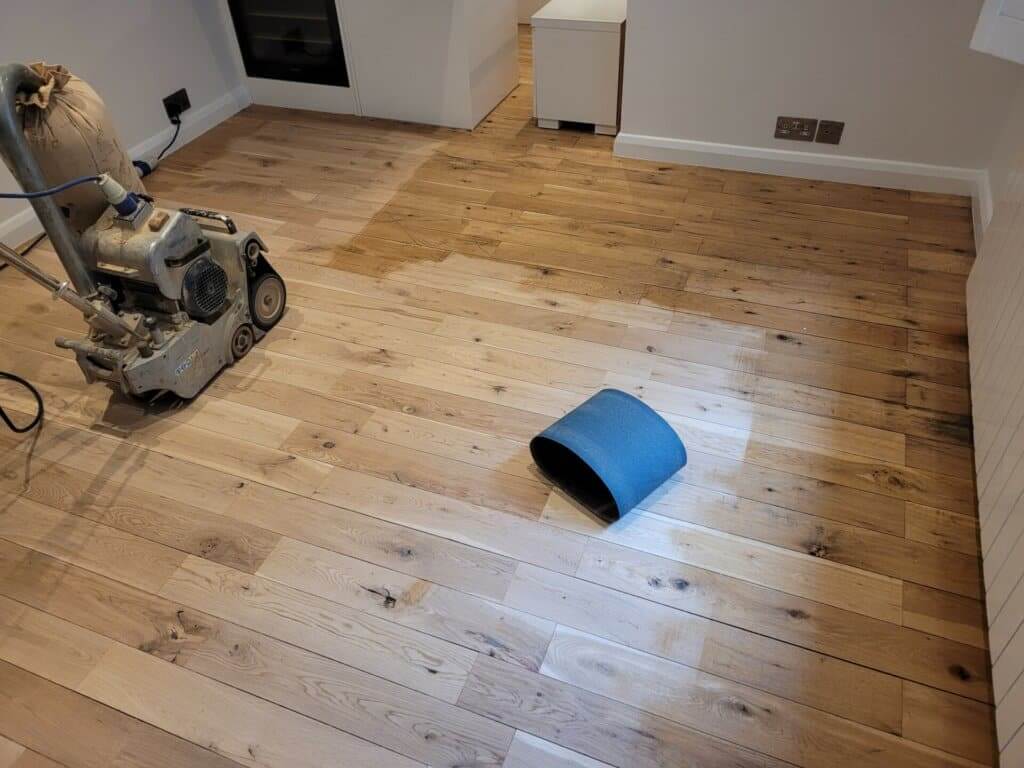 A professional from Mr Sander® is sanding a solid oak hardwood in a living room in Cudham, UK using a Bona Belt sander (AMO110000.3). The machine features a 2.2 kW motor, 230 V voltage, 50 Hz frequency, and a sanding belt size of 200 x 750 mm or 250 x 750 mm. The total weight is 74 kg.