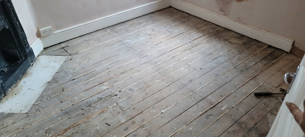 An old, worn wooden floor in a room with debris and a hammer, indicating a renovation in progress.