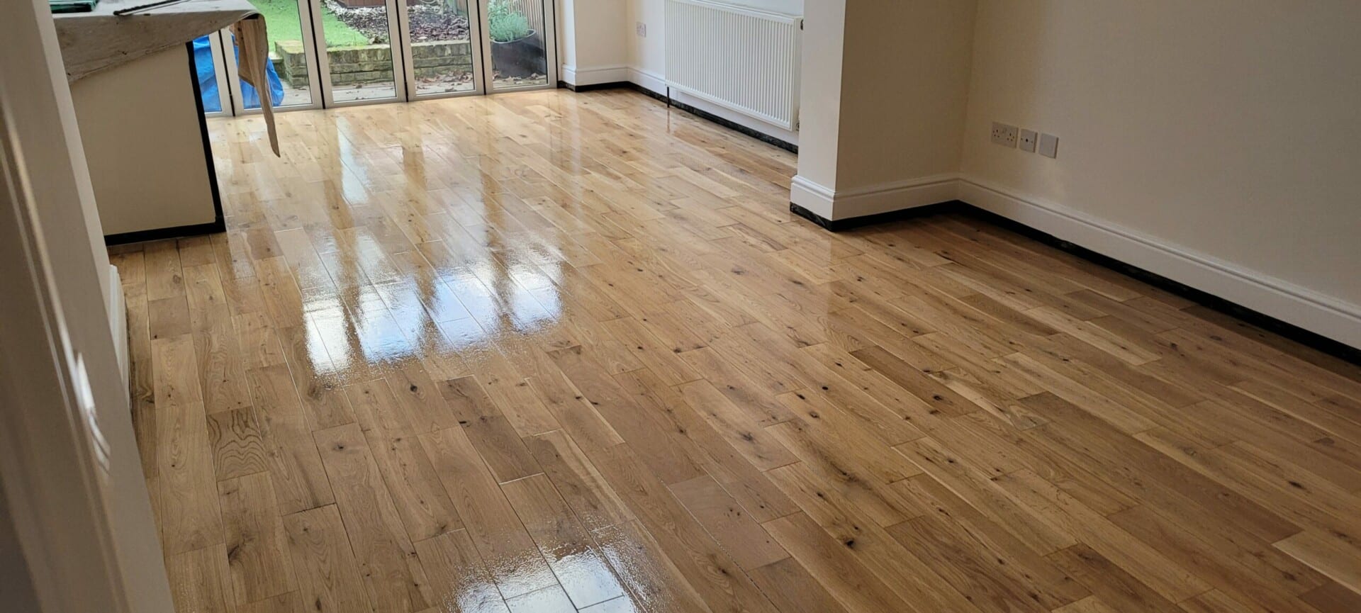 Shiny wooden flooring extending from a kitchen area to a room with glass doors leading to the outside.