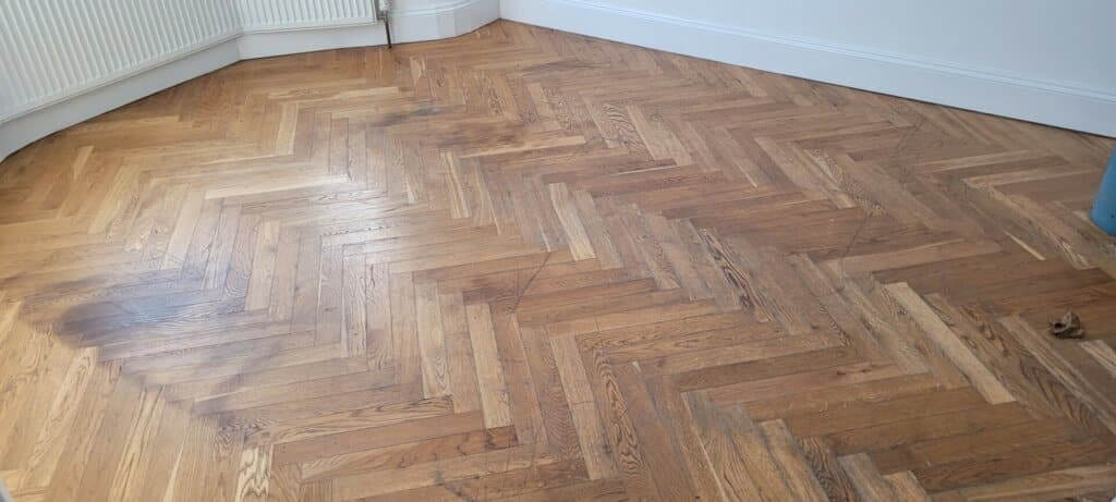 A partially sanded parquet floor in a residential room showing the difference between the worn and freshly sanded sections. The floor sanding and refinishing work is being done by Mr Sander®, highlighting the restoration process.