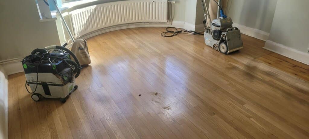 An oak floor in a living area in Mitcham, UK, sanded by Mr Sander® using Bona Belt sanders (AMO110000.3) and Bona DCS 50. The Bona Belt sander features a 2.2 kW motor, 230V, with a sanding belt size of 250x750 mm, weighing 74 kg. The Bona DCS 50, with 1380 W motor power, 51 L dust capacity, and Teflon coated pre-filter, ensures efficient dust containment.