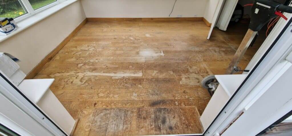 A worn and damaged wooden floor in a sunroom, ready for sanding and refinishing by Mr Sander®. The image shows various marks and discolorations on the floorboards, indicating the need for professional restoration.