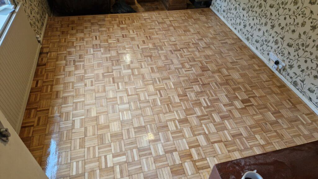 A beautifully restored parquet flooring in a living room with a glossy finish. The floor sanding and refinishing were performed by Mr Sander® in West London, UK, highlighting the intricate pattern and smooth surface of the oak parquet tiles.