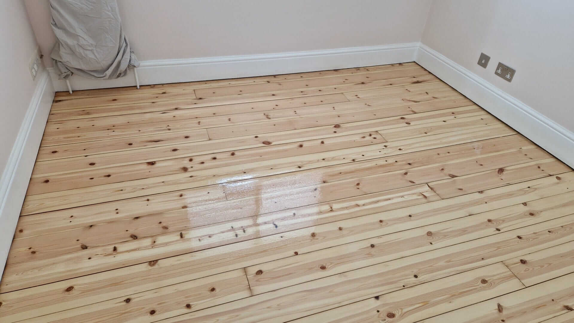A newly sanded and refinished wooden floor in Chadwell Heath, UK, done by Mr Sander®. The image shows a close-up view of the light-coloured, polished wooden floorboards.