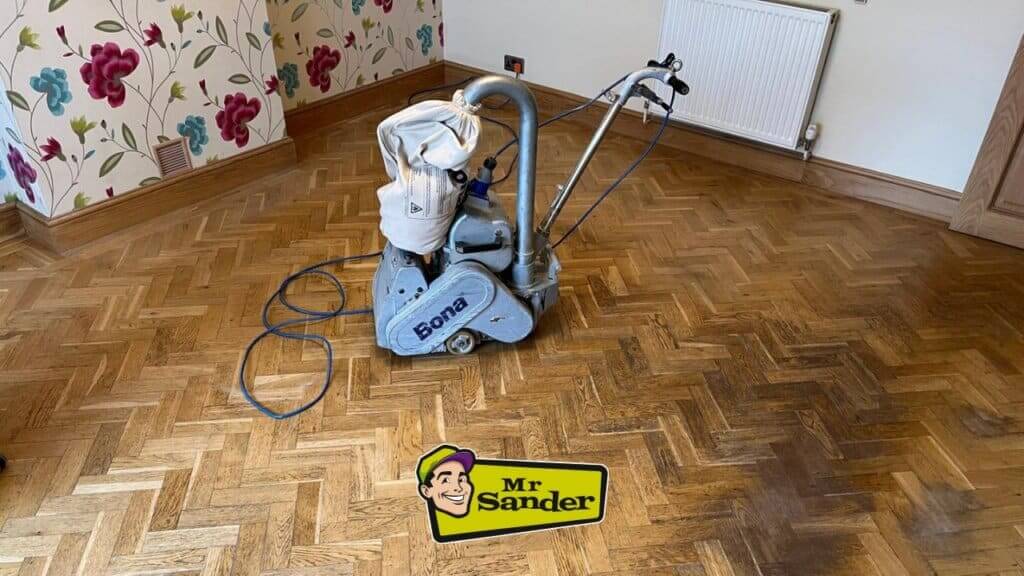 A Bona floor sander is being used to sand a herringbone parquet floor. The Mr. Sander® logo is in the bottom right corner.