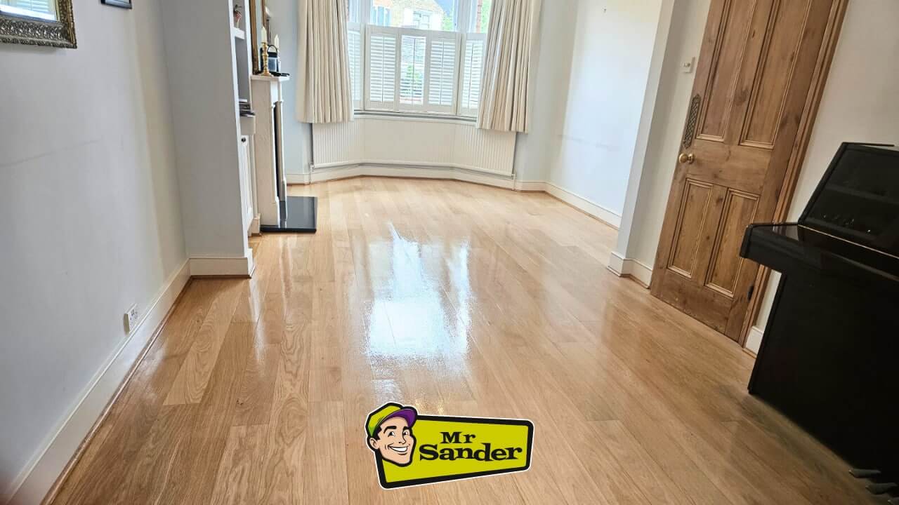 A beautifully restored living room with a polished wooden floor. The room features a bay window, white walls, and a wooden door, with the Mr Sander® logo displayed at the bottom.