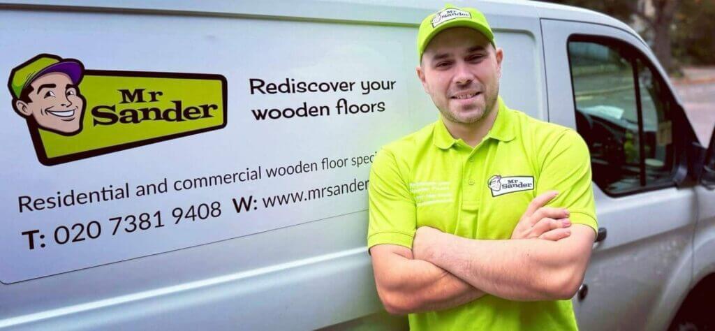 A professional floor specialist, Mr. Sander, stands confidently in front of his branded van, which displays the company logo and contact information. He is wearing a bright green uniform and cap, ready to provide residential and commercial wooden floor services.