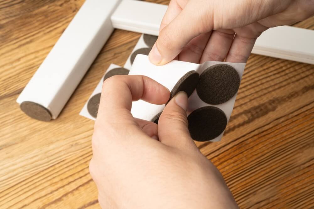 Hands applying felt pads to furniture legs to protect a newly refinished wooden floor from scratches.
