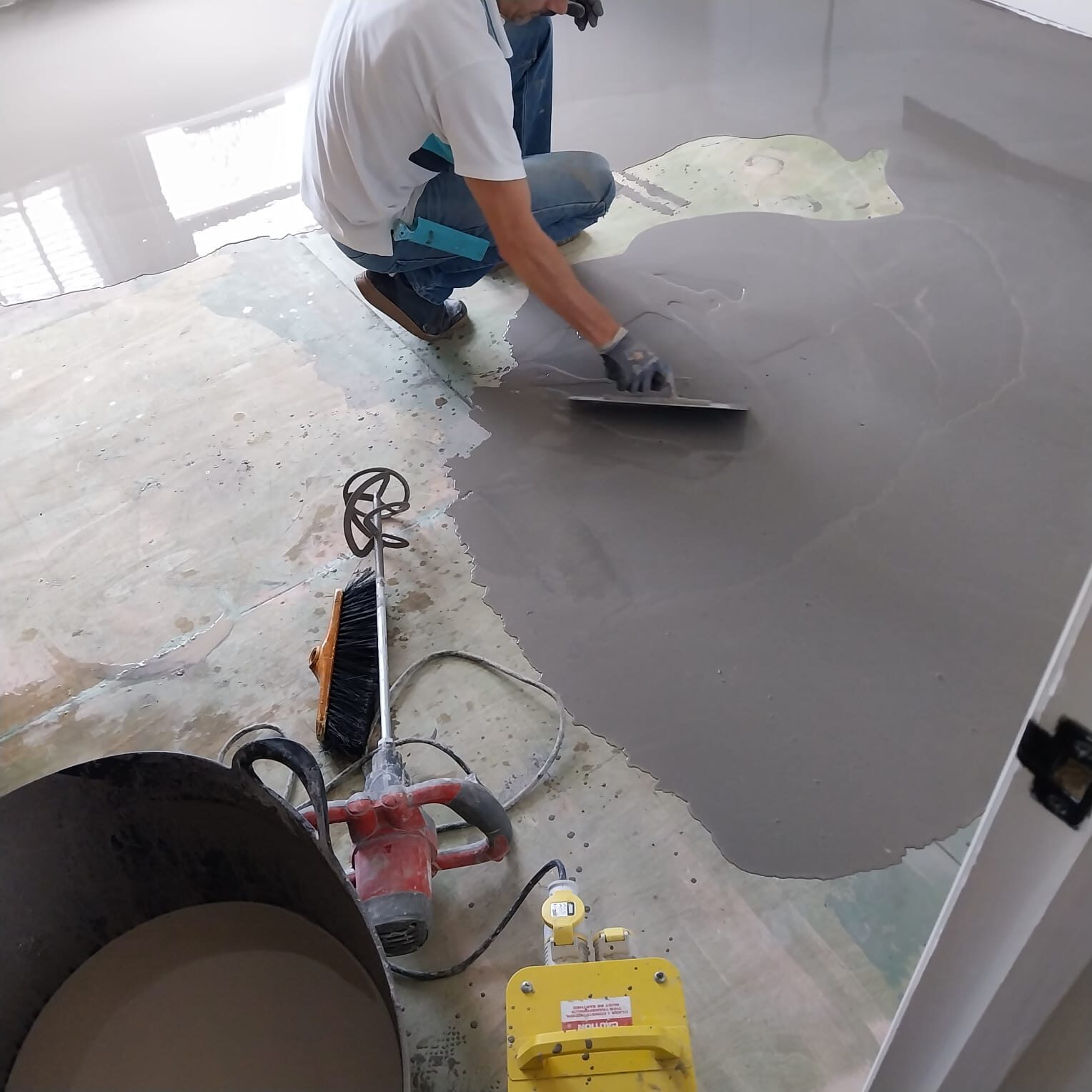 Self-levelling compound being trowelled to correct an uneven subfloor before underlay—evidence for 5 Underlay Myths that underlay can’t fix flatness issues; preparing for oak herringbone engineered parquet (engineered wood).