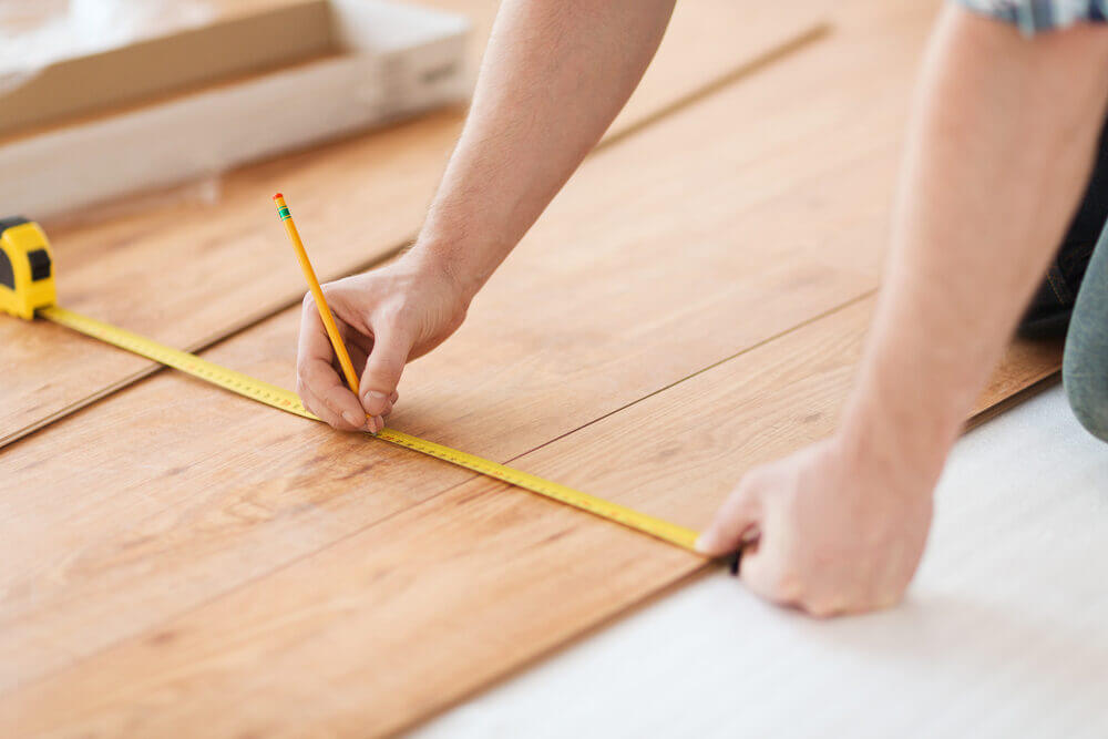 A pair of hands using a tape measure and pencil to mark wooden planks, demonstrating meticulous preparation for West London Floor Fitting.