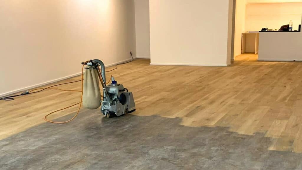 A professional from Mr Sander® using a Bona Belt sander (model AMO110000.3) to sand a floor in a living area in the UK. The belt sander has an effect of 2.2 kW, operates at 230 V and 50 Hz, and measures 250x750 mm. The drum width is 200 & 250 mm, and the sanding belt size is 200 x 750 mm or 250 x 750 mm. The motor power is 2.2 kW, and the total weight of the machine is 74 kg.