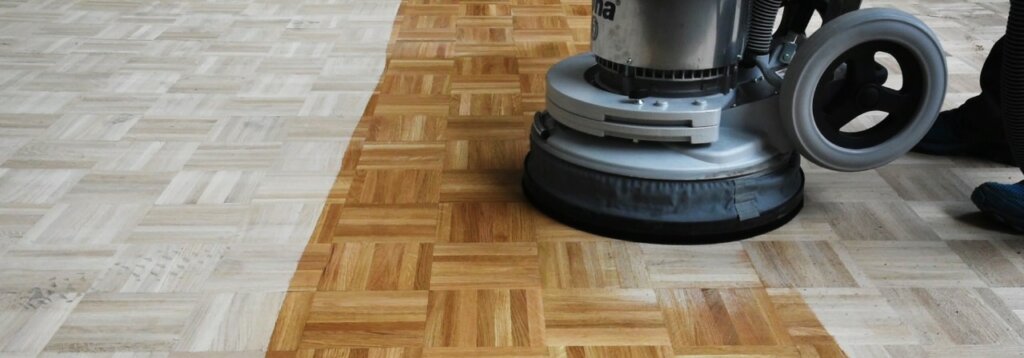A Mr Sander® technician sands a parquet floor in a Belvedere, UK living room using a Bona FlexiSand 1.9 (AMO310002). The machine features a 1.9 kW motor, 230 V, 50 Hz, with a 407 mm diameter disc. It includes a 16 A overload switch, thermal protection, and weighs 50 kg. Abrasive disc speed is 147 rpm.