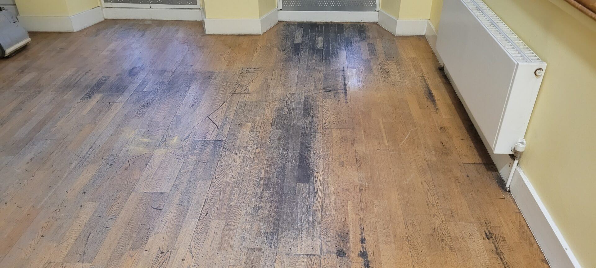 Before photo of a heavily scratched wooden floor in need of repair, illustrating the necessity for effective solutions for scratched wooden floors.