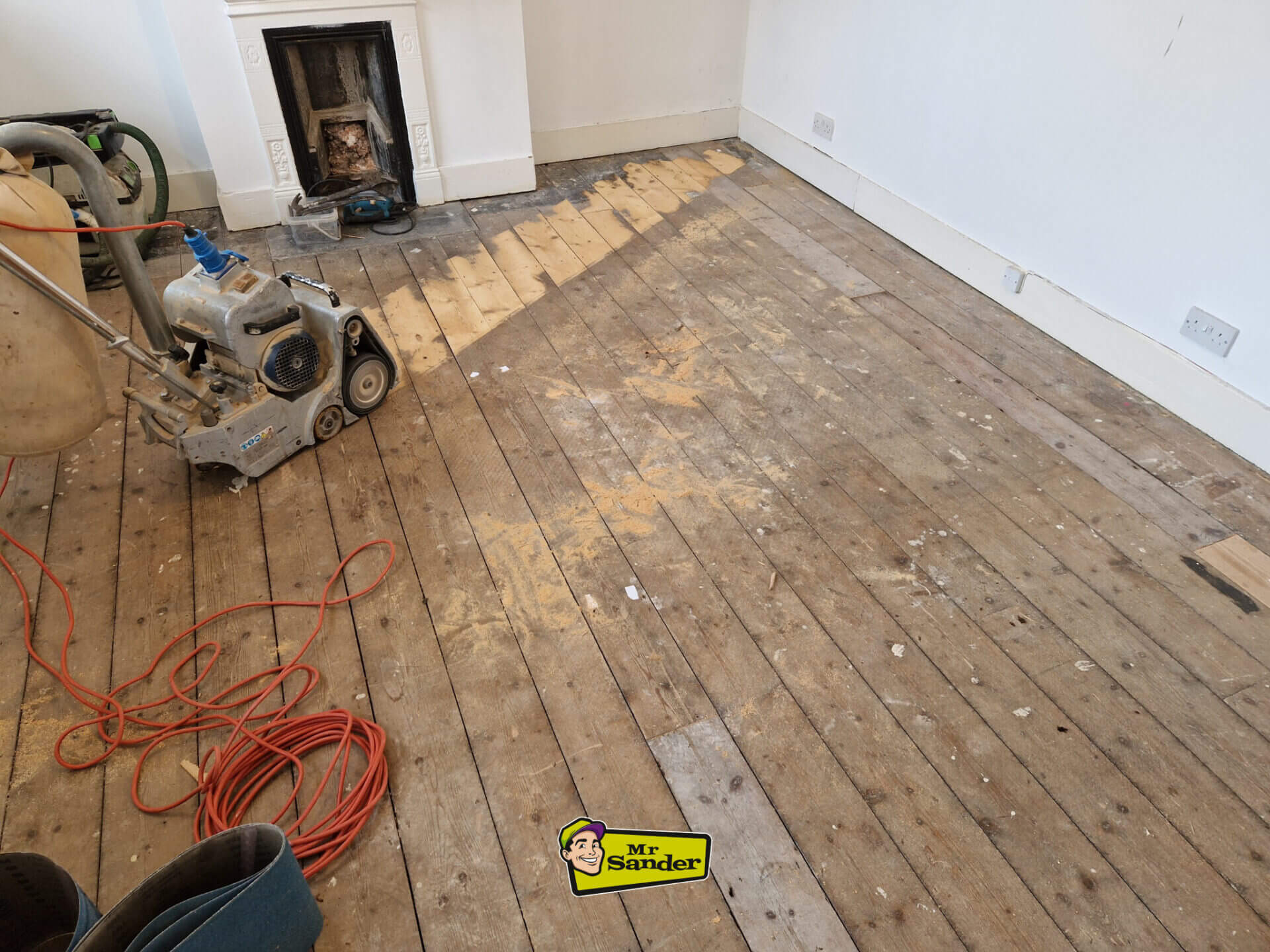 Partially sanded pine floor in a living room, revealing brighter boards as the old finish is removed by a professional sanding machine.