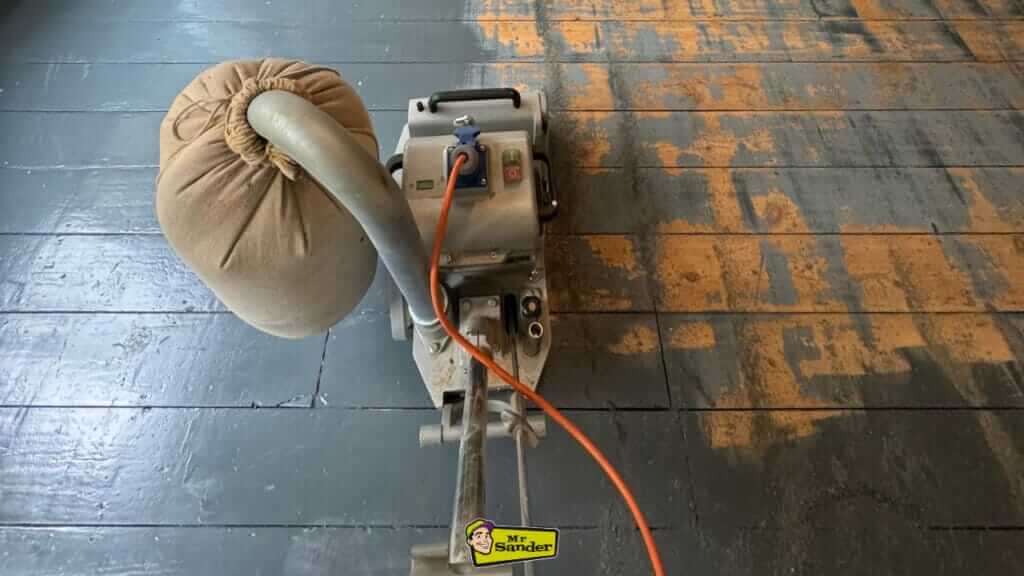 A floor sanding machine in action removing old paint from wooden floorboards, showcasing the restoration process.