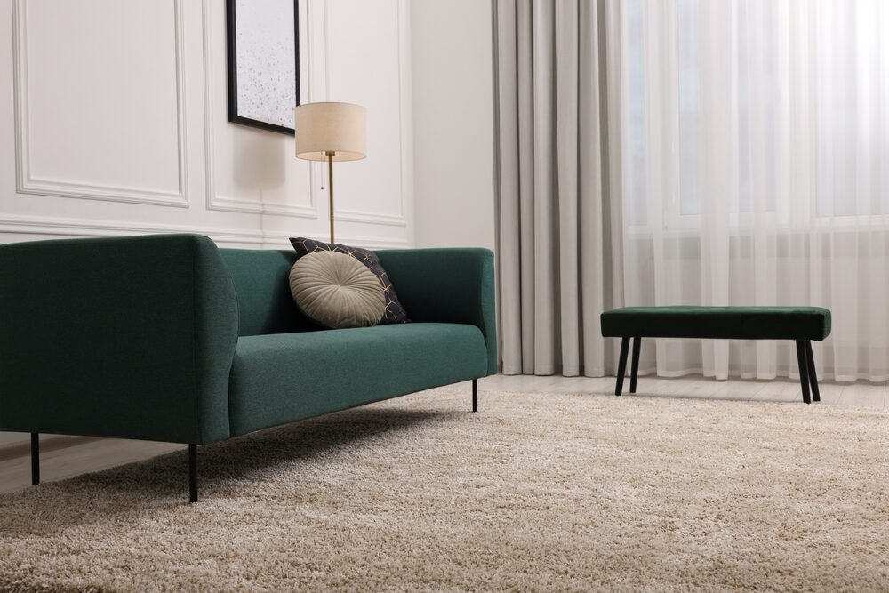 A modern living room featuring a plush green sofa, matching ottoman, and a large beige carpet that contrasts with potential Wood Floor Fitting options.