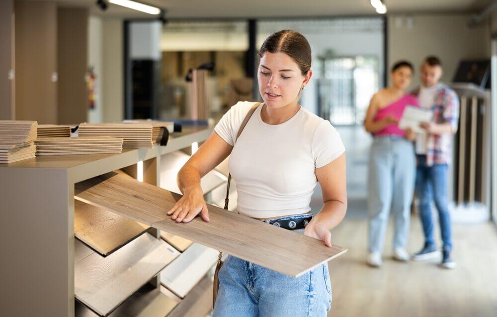 A young woman examining a wood plank in a flooring showroom, demonstrating the selection process for a West London Floor Fitting project.