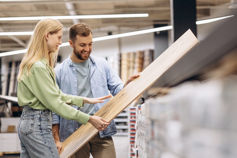 A couple evaluating a sample plank of laminate flooring in a DIY store, reflecting the selection process for an upcoming Laminate Floor Installation.