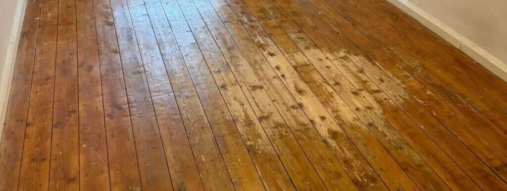 A worn wooden floor with visible patches of damage and uneven finish, captured before professional refinishing by Mr Sander®.