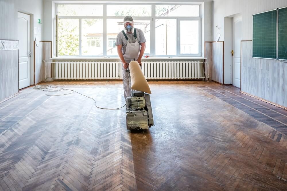 A professional from Mr Sander® is sanding a living room floor in, UK, using a Frank Cobra Belt Sander. The high-powered, dust-free machine weighs 78kg and features a 2500W motor, 2100rpm sanding speed, and 200x750 endless belt. The Frank Cobra offers quick belt changes, integrated DCS for 99.99% dust extraction, featherlite clutch control, and automatic belt adjustment. Ideal for professional sanding and stripping of all wooden floors, including parquet.