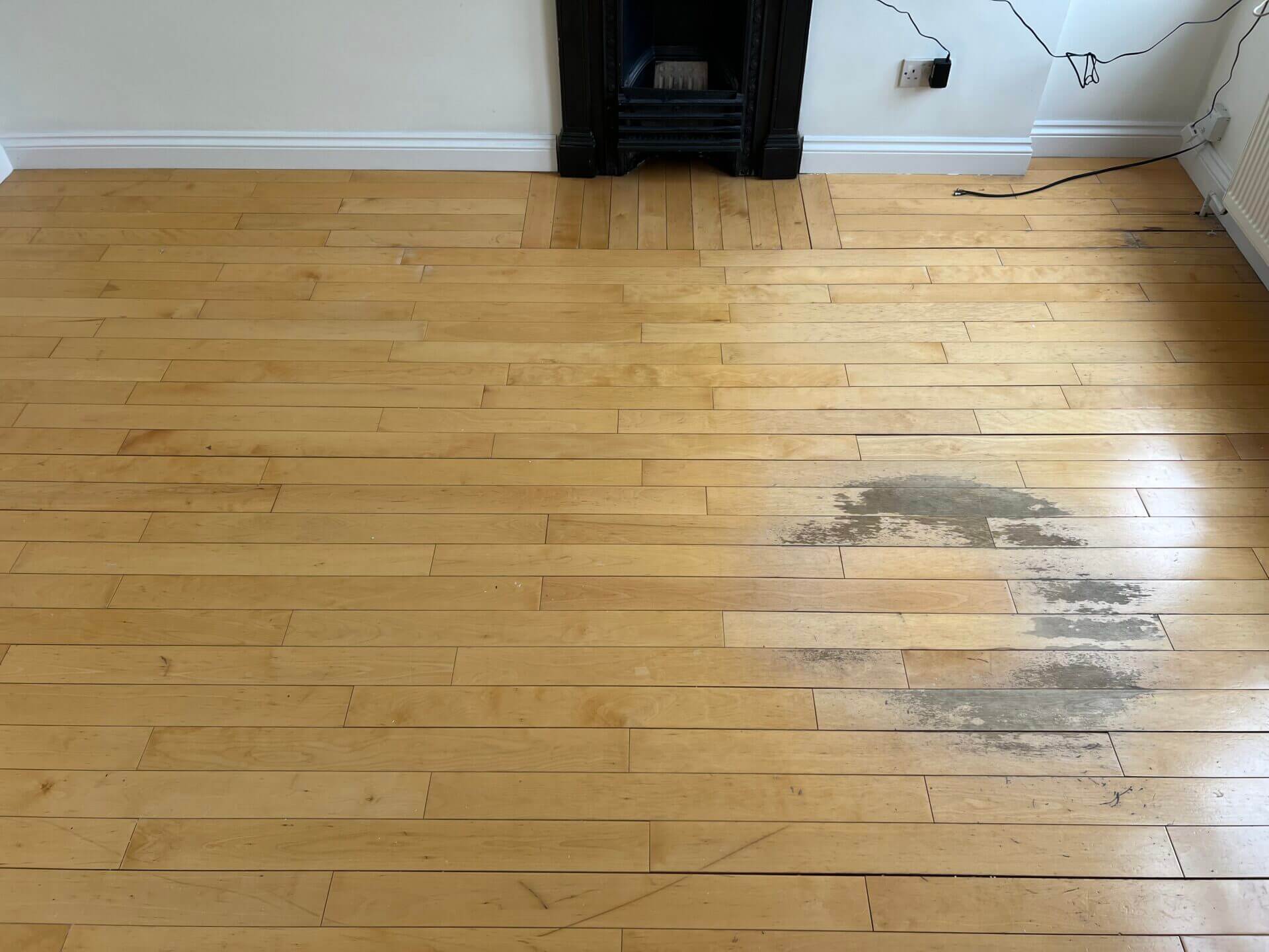 Living room hardwood floor with visible stains and wear, illustrating the need for Floor Sanding for Hardwood Floors.