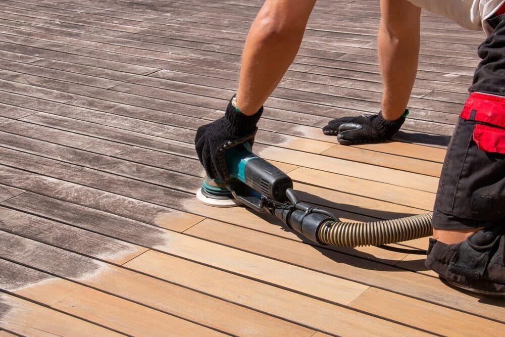 Person applying stain to wooden deck boards with a brush, creating a refreshed appearance.