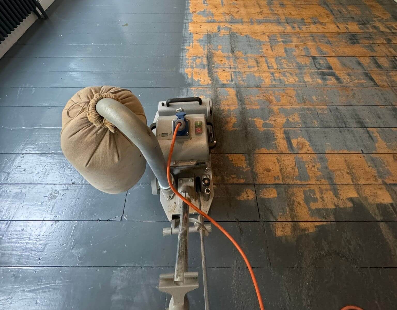 A professional floor sander removing paint from a wooden surface, demonstrating the answer to “Does Sanding Floors Remove Paint?