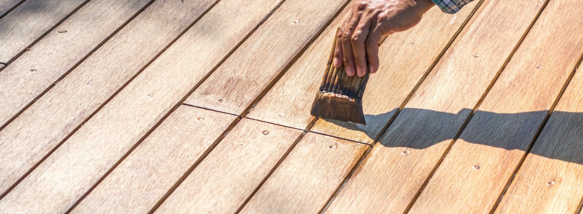 A person with a brush on a wooden deck. 