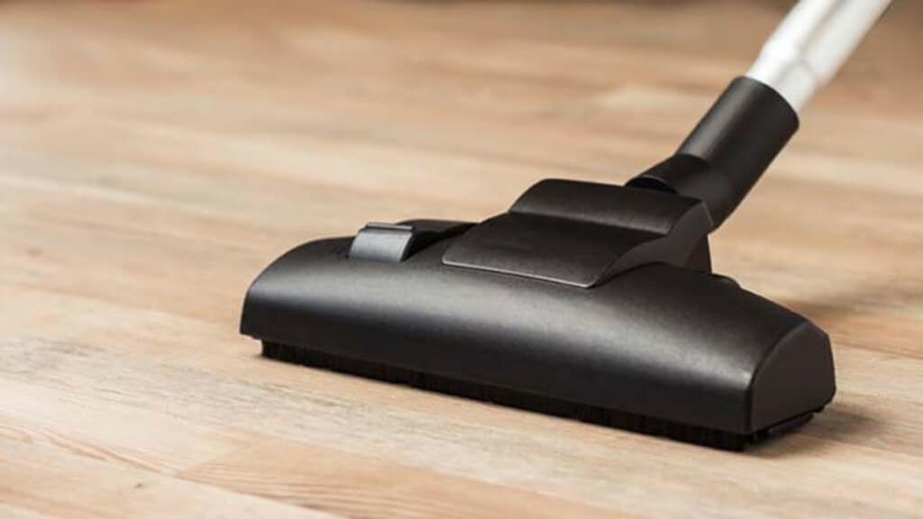 A close-up of a vacuum cleaner head being used to clean a hardwood floor. The floor appears smooth and polished, indicating it has recently been sanded and refinished.