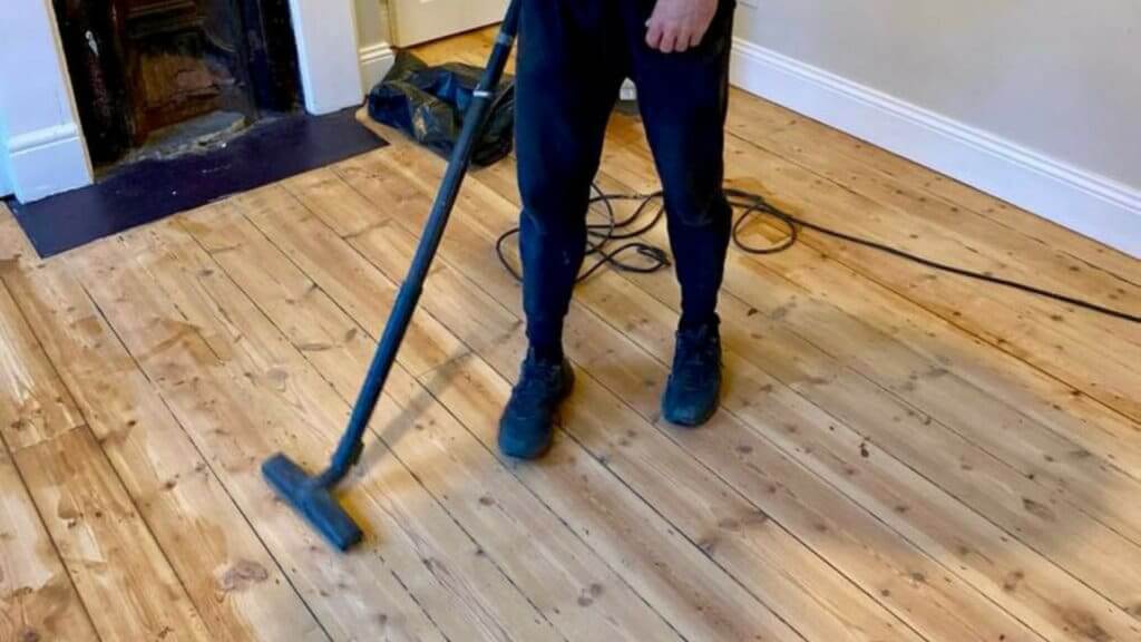 A professional using a vacuum to clean a newly sanded wooden floor. The image shows the technician's lower half, emphasizing the smooth, even surface of the floor and the thorough cleaning process that follows sanding. This highlights the meticulous floor sanding and refinishing services provided by Mr Sander®.