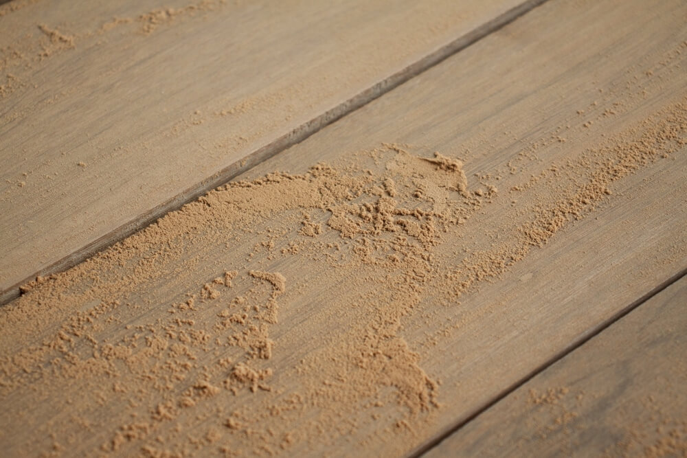 Close-up of dust scattered on a hardwood floor during a floor sanding process. The image showcases the unfinished surface of wooden floorboards after partial sanding, with sawdust accumulating in some areas.
