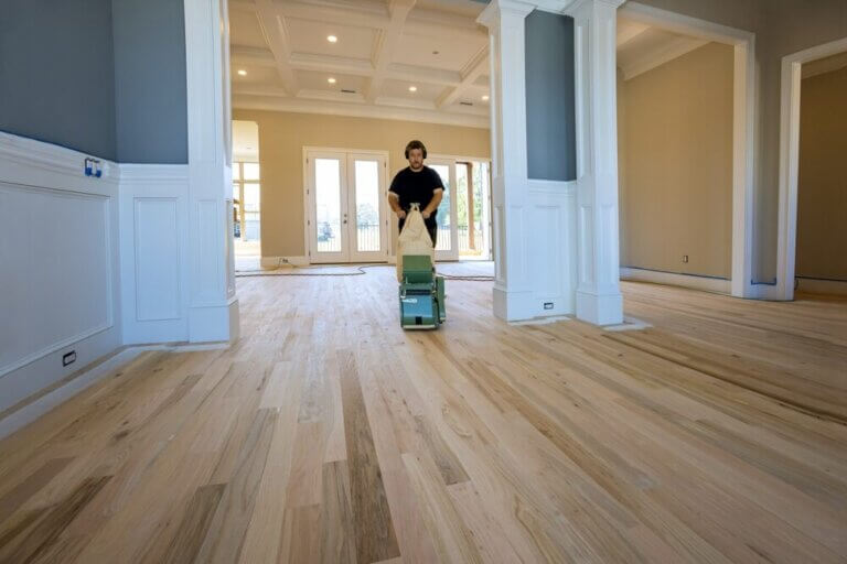 Professional floor sanding technician operating a sanding machine on hardwood flooring in a large open living area, illustrating Floor Sanding for Hardwood Floors.