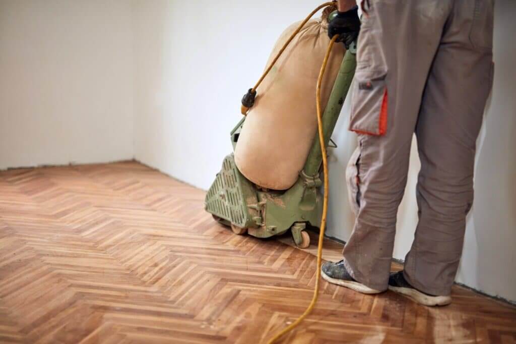 A professional floor sanding specialist using a sanding machine to restore a herringbone parquet wood floor.
