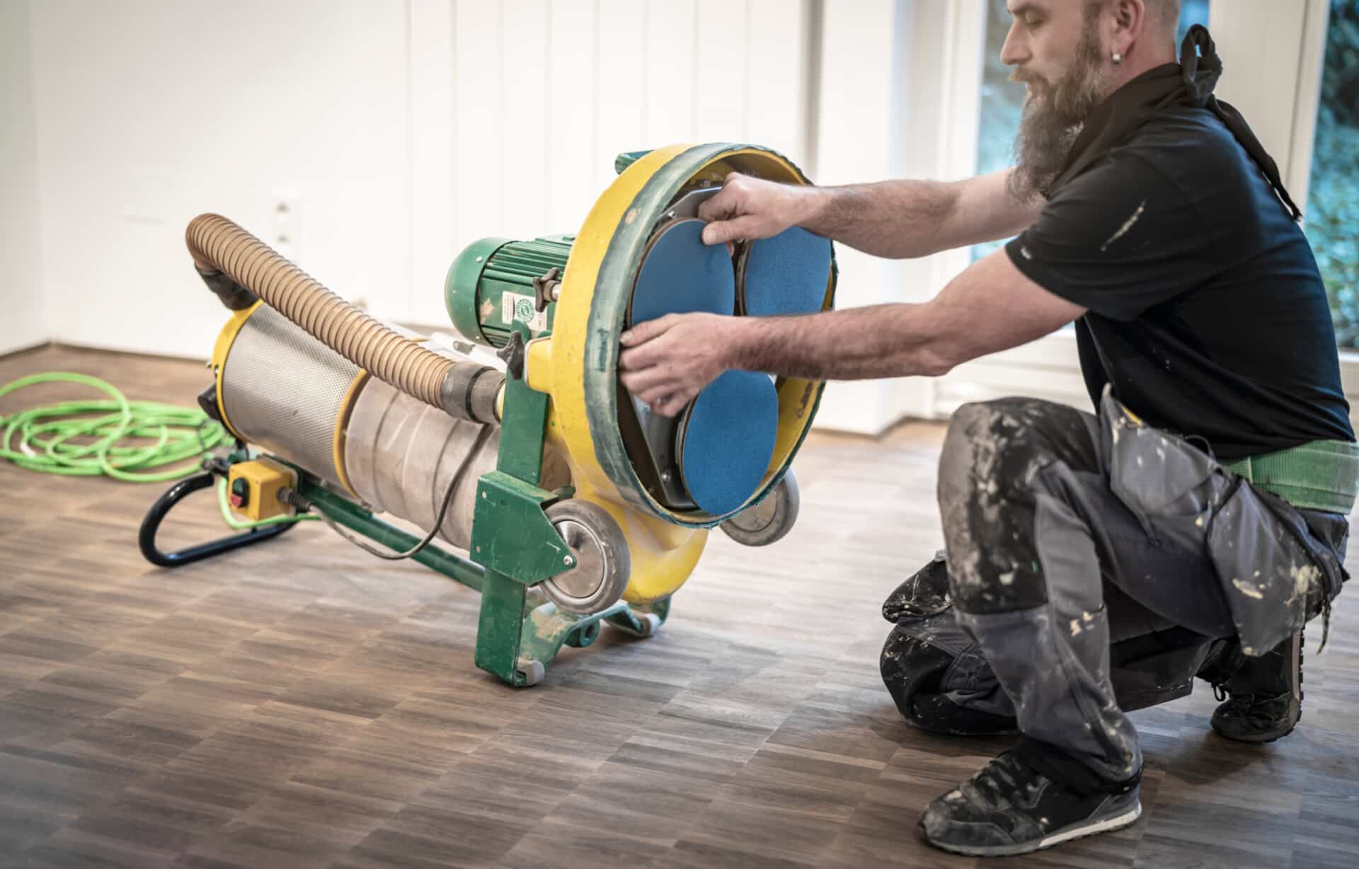 A floor sanding technician changing sanding discs on a Dust-Free Floor Sanding System while working on an engineered wood floor in a residential home.