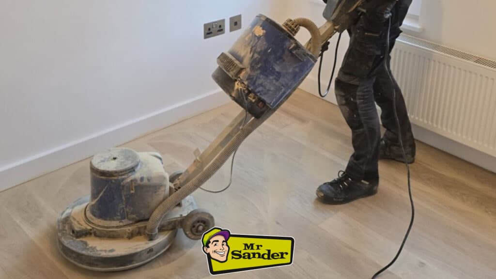 Professional sanding machine in action, operated by a skilled technician restoring a light wood floor, with visible dust and a near-complete surface.