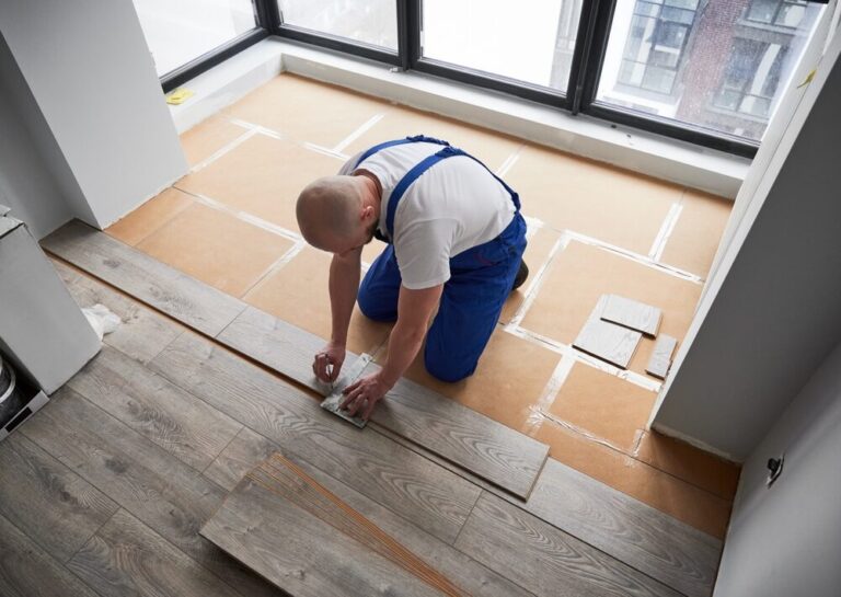 A professional installer kneeling on an underlayment, measuring grey laminate planks for a precise Floor Fitting and Installation in a modern UK apartment.