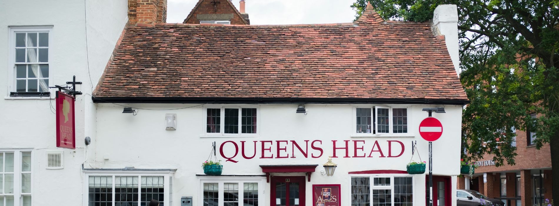A white wooden-floored building in Aylesbury, HP21, features a prominent red sign displaying "Queen's Head," adding a touch of character to the establishment.