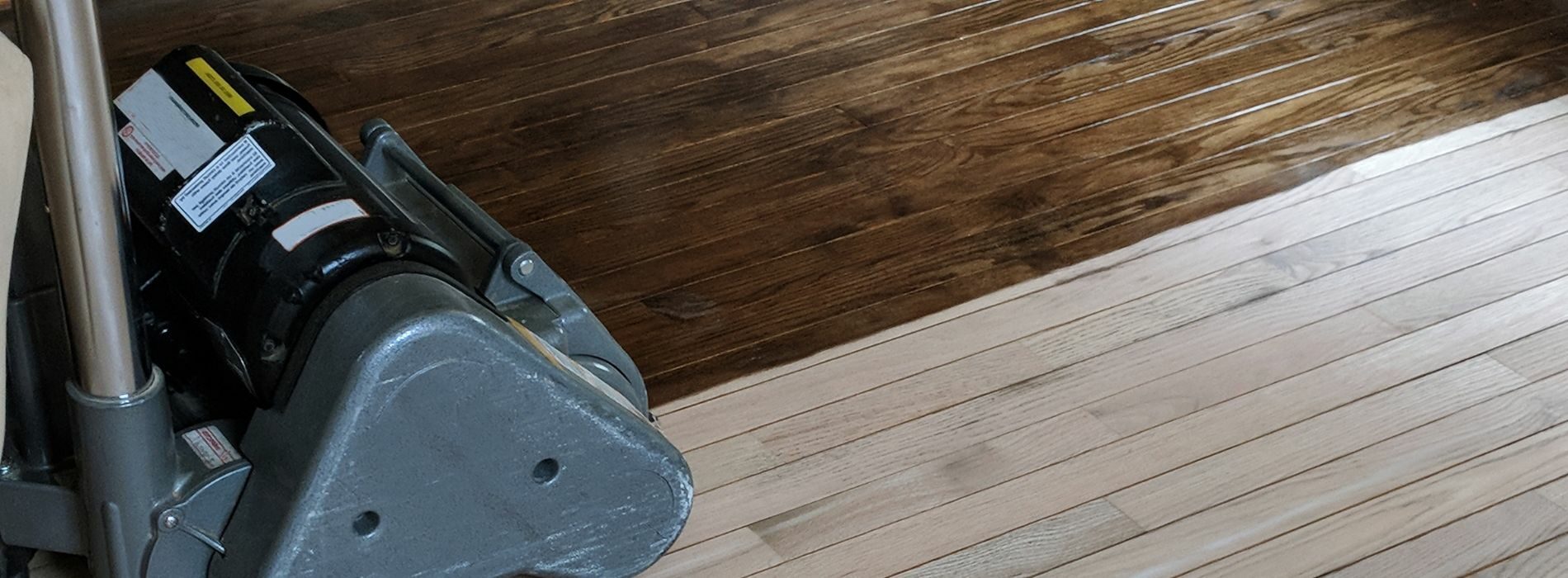 A detailed close-up of a vacuum cleaner placed on a beautifully finished wooden herringbone floor. The vacuum is part of the floor sanding process carried out by the Mr Sander®. It is connected to a dust extraction system with a HEPA filter to ensure a clean and efficient sanding result. The vacuum's nozzle is positioned near the floor surface, ready to capture and remove any dust and debris generated during the sanding process. The wood's rich color and the intricate herringbone pattern are visible, adding to the overall aesthetic appeal of the image