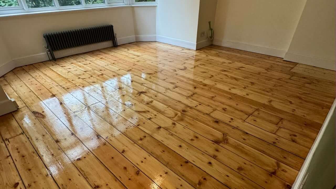 A beautifully restored wooden floor with a polished finish, reflecting natural light from large windows in a bright, cozy room.