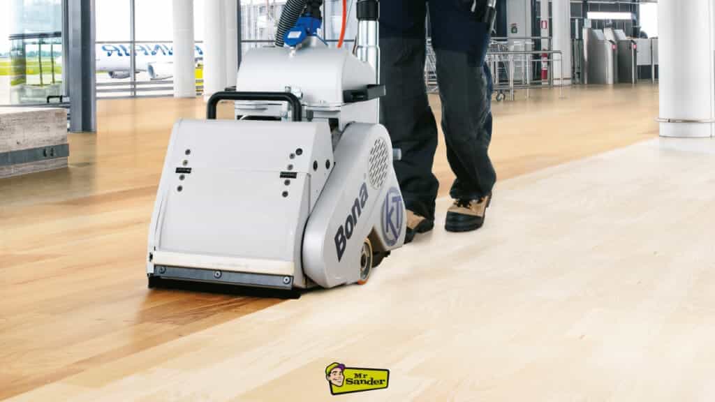 A professional technician operating a Bona sanding machine on a large, polished wooden floor in a commercial setting.