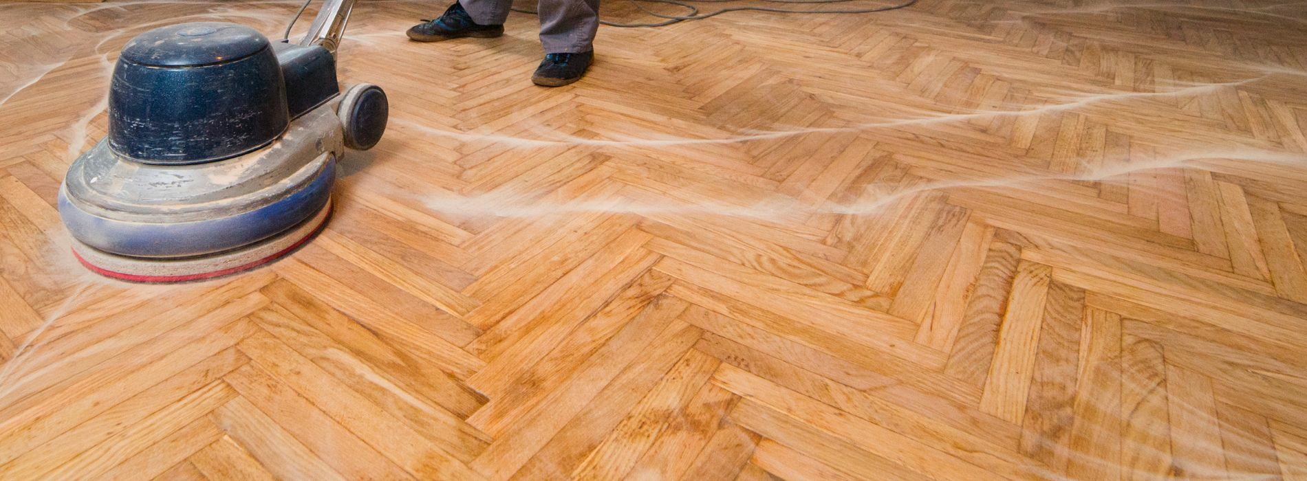 A skilled professional wearing protective gear operates a high-powered 540v polishing machine with a 750mm driving plate and a 60grit screen to meticulously restore the luster of a beautiful parquet floor. The expertly controlled machine effortlessly glides over the wooden surface, revealing a flawless finish. The intricate patterns of the parquet floor shine under the careful attention, reflecting light and showcasing its natural beauty.