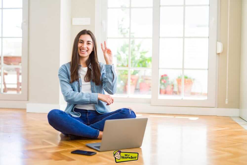 A happy Garthamlock G33 customer sitting on a newly refinished wooden floor, showcasing professional floor restoration by Mr Sander®️.