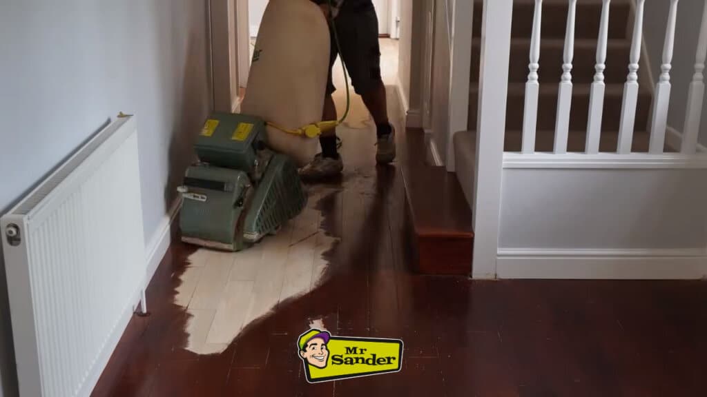 Professional sanding machine restoring hallway floorboards in Doune (FK16), illustrating the contrast between original and sanded surfaces.